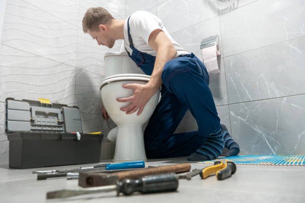 Man plumber in uniform installing toilet bowl